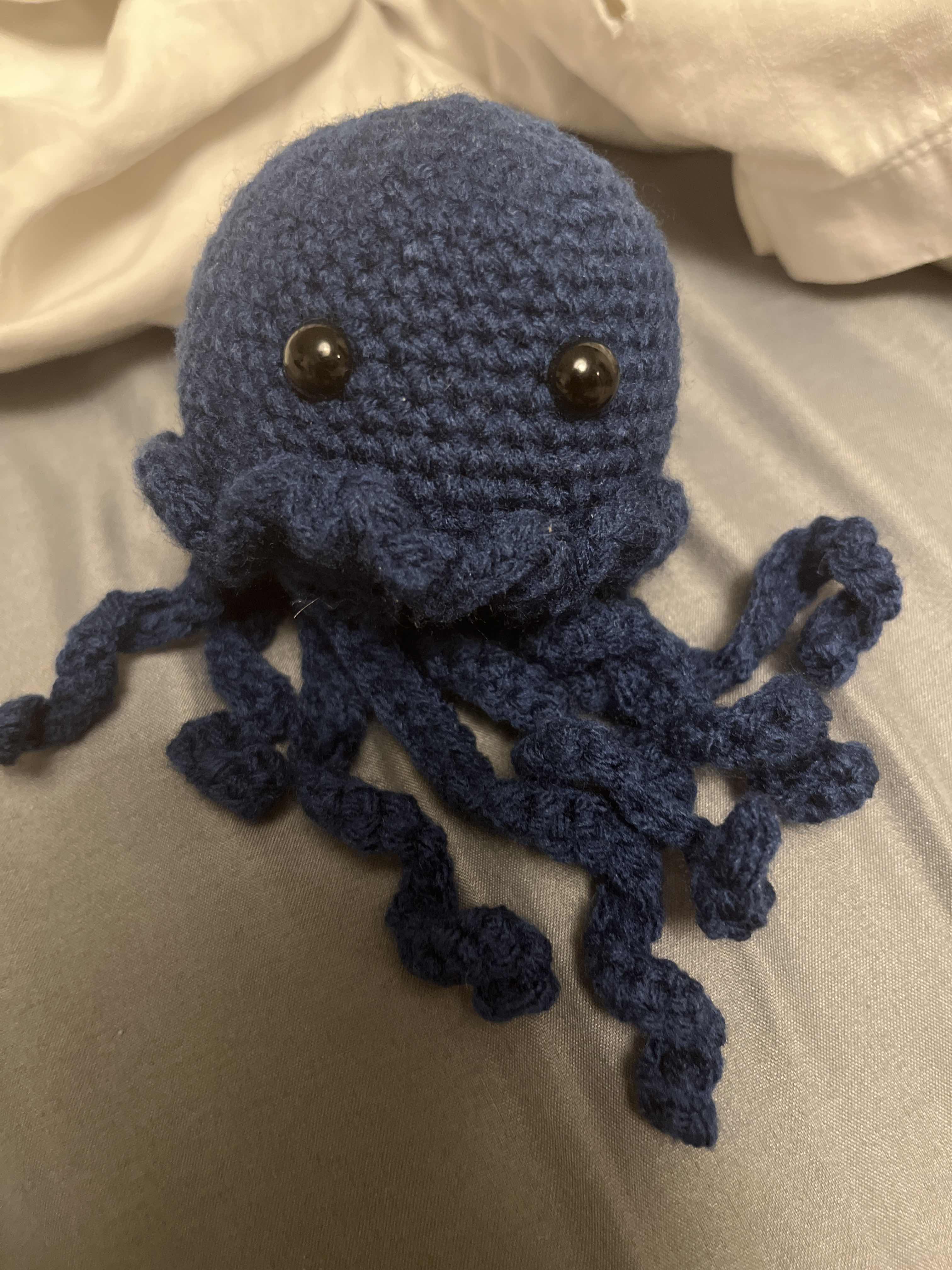 A picture of a crocheted blue jellyfish with black eyes.