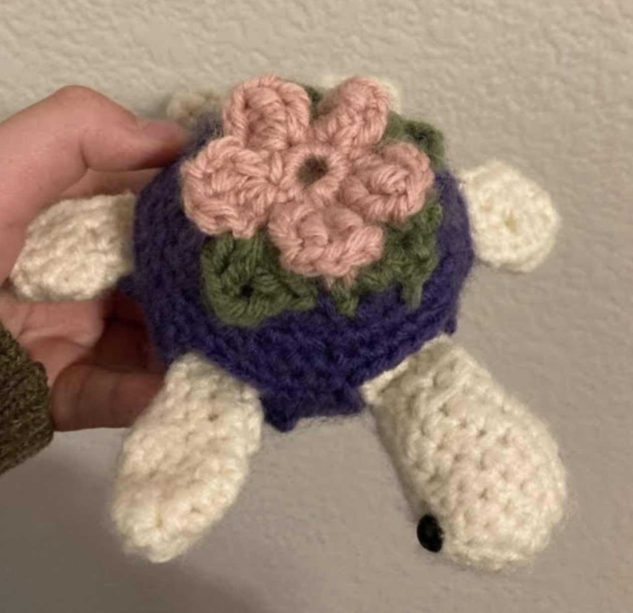 A picture of a hand holding a small crocheted turtle with a flower on its back